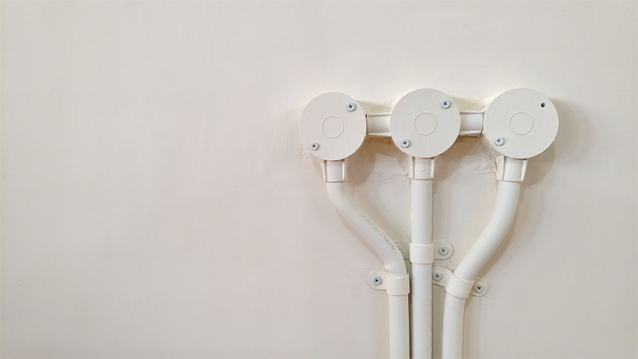 Three electrical junction boxes with PVC electrical conduit neatly installed on white wall